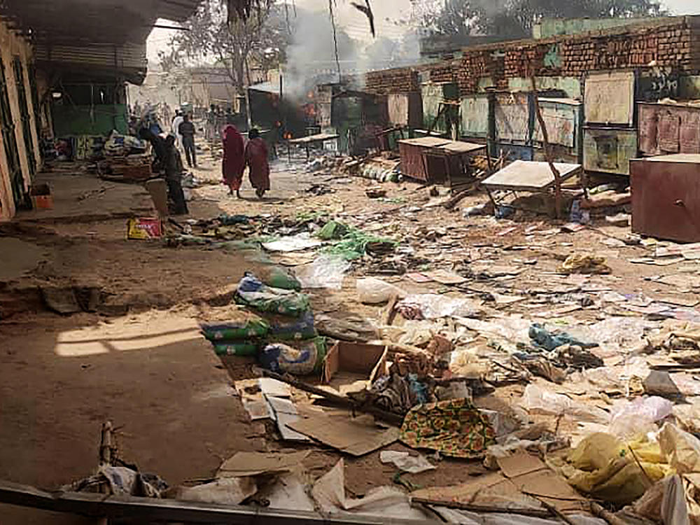 People walk among scattered objects in the market of El Geneina, the capital of West Darfur, as fighting continues in Sudan between the forces of two rival generals, on April 29, 2023.
