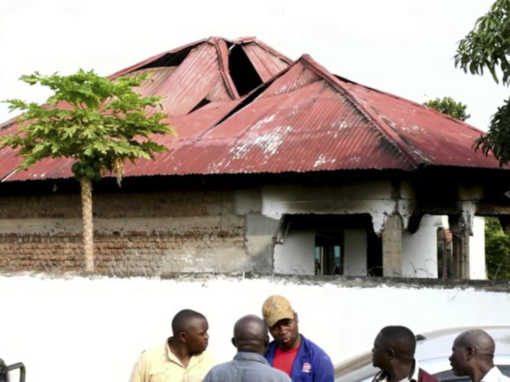 In this image made from video, people gather on Saturday in front of a building of the Lhubiriha Secondary School  Mpondwe, Uganda, near the border with Congo following an attack on the school.