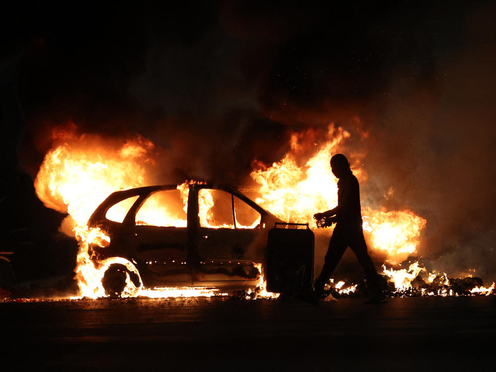 A man walks by a burning car during clashes with police in Le Port on the French Indian Ocean island of La Reunion, on Friday over the fatal shooting by police of a 17-year-old in a Paris suburb.