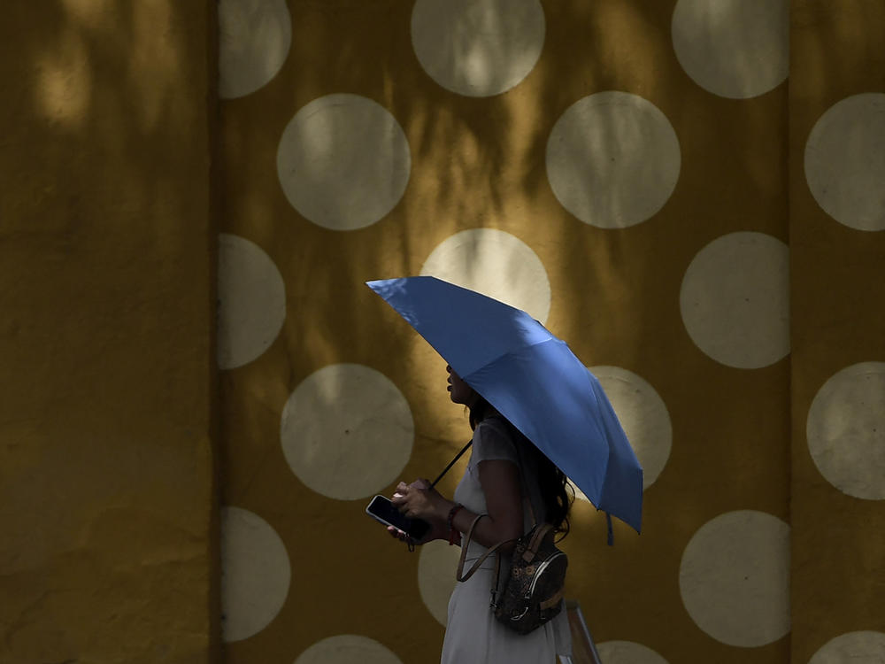 A pedestrian covers her head with an umbrella while walking during a heatwave in Seville, Spain on Monday.