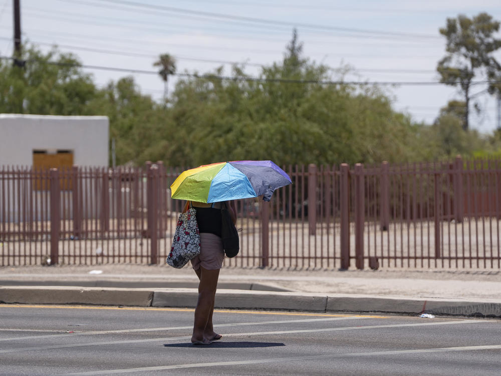 A person shields themselves from the sun with a rainbow umbrella during a heat wave in Tucson, Ariz., on Saturday.