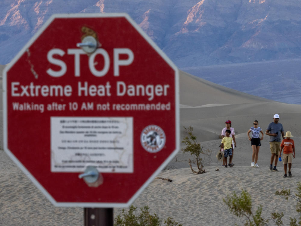 People walk among sand dunes near a sign warning of extreme heat danger in Death Valley National Park on Saturday.