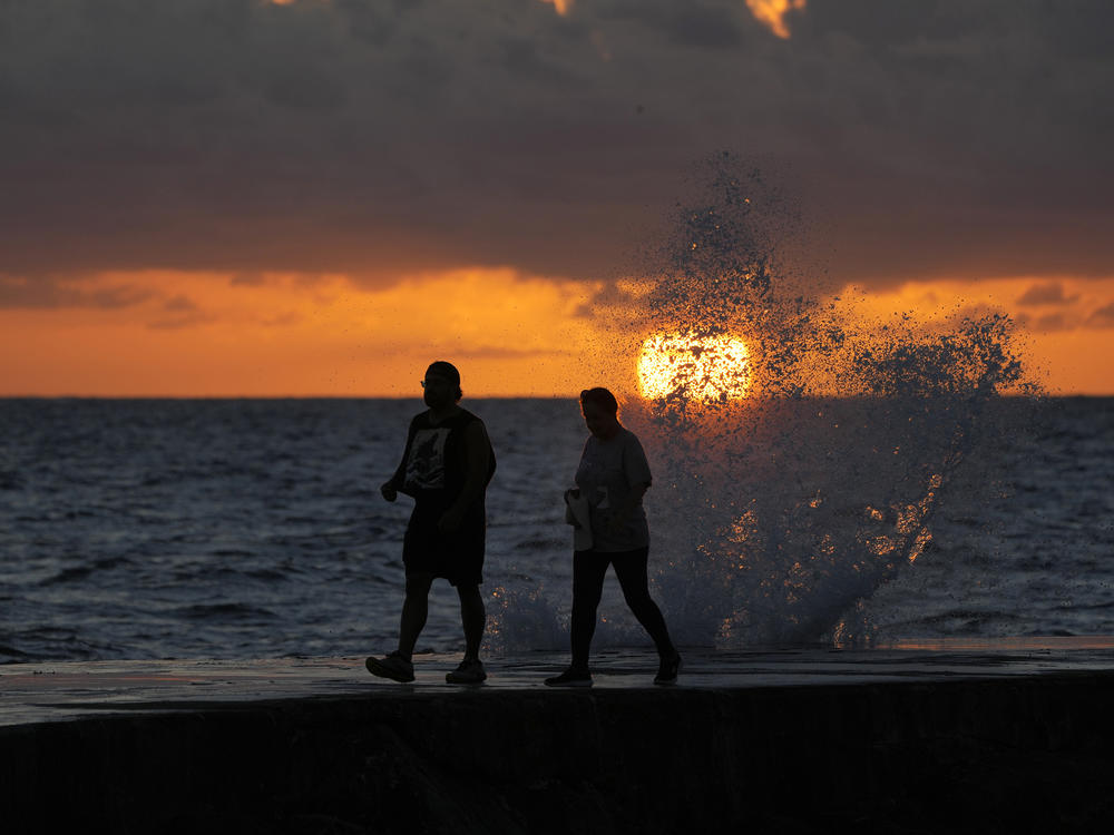 The sun rises above the Atlantic Ocean as waves crash near beach goers walking along a jetty, Wednesday, Dec. 7, 2022, in Bal Harbour, Fla. (AP Photo/Wilfredo Lee)