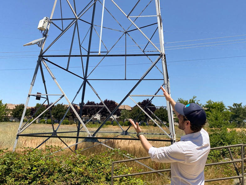 Jon Marmillo gestures at a box full of laser sensors on a transmission tower in Folsom, Calif. The sensors can read things like wind and temperature and give that data to utilities so they can safely transmit more power.