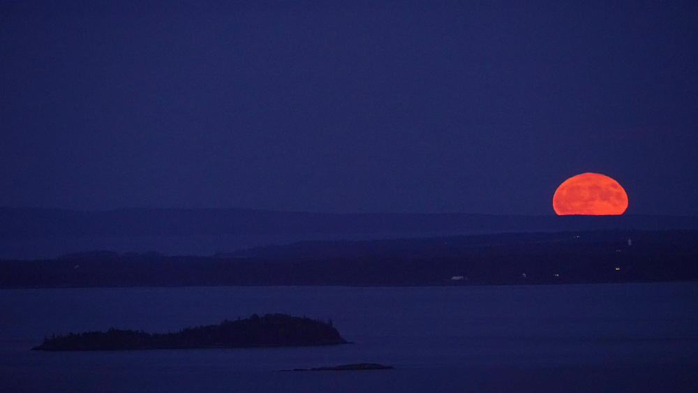 The supermoon ascends into the sky with Isle au Haut in the distance and North Haven Island in the middle ground, as viewed from Camden, Maine.