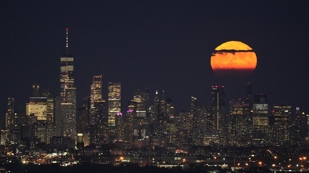 The moon shines through clouds over the lower Manhattan skyline, as seen from New Jersey.