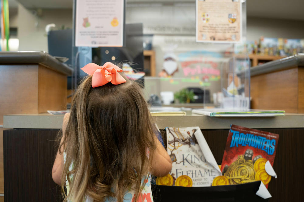 A young girl checks out her selection of books at the Livingston Parish Library Main Branch in Livingston, La. She's among those disappointed that all libraries in the parish are now closed on Sundays.