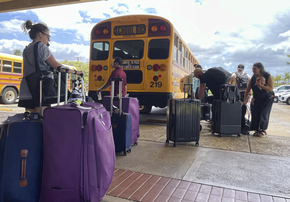 People wait with their luggage at the Maui airport in Kahului, Hawaii, on Thursday as school buses continue shuttling people over from the west side of the island.