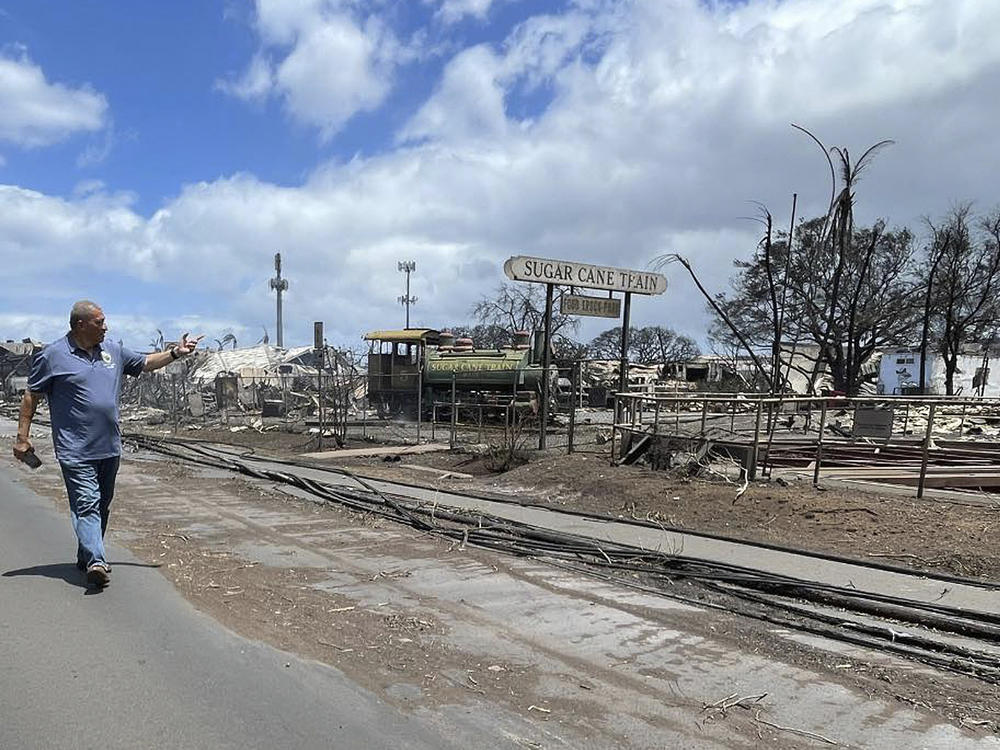 In this photo released by the County of Maui, Lahaina Mayor Richard Bissen walks past the remains of the Sugar Cane Train depot on Thursday, Aug. 10, 2023. Authorities in Hawaii are working to evacuate people from Maui as firefighters work to contain wildfires and put out flare-ups. (County of Maui via AP)