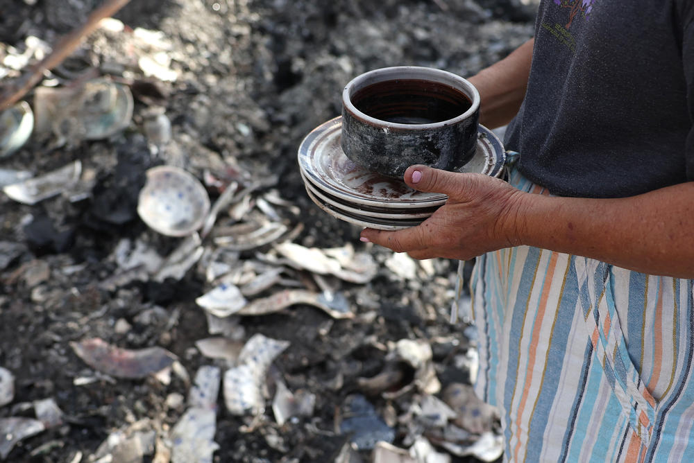A resident holds a stack of dishes that were salvaged from the rubble of a home that was destroyed by wildfire on August 12 in Kula, Hawaii.