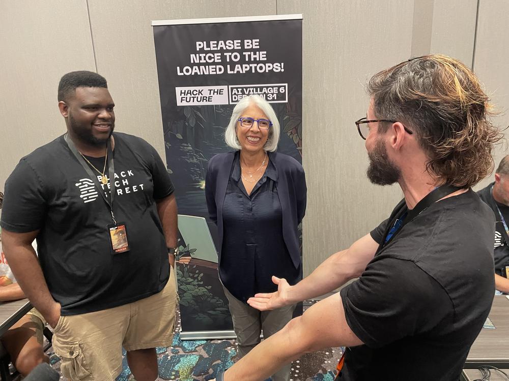 Arati Prabhakar of the White House's Office of Science and Technology Policy talks with Tyrance Billingsley (left) of Black Tech Street and Austin Carson (right) of SeedAI, about the AI challenge.