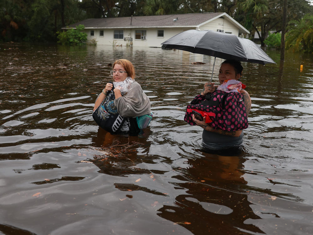 Makatla Ritchter and her mother, Keiphra Line, wade through flood waters after evacuating their home in Tarpon Springs, Florida. Flood waters from Hurricane Idalia inundated it on August 30, 2023. Climate change is making storm surge and intense rainfall during hurricanes like Idalia more dangerous.