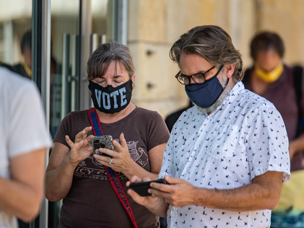 Voters check their phones while waiting to cast in-person ballots at a polling location in Austin, Texas, on Oct. 13, 2020. Many Americans wonder why they can't vote online, on their phones, but experts agree that it's not secure.