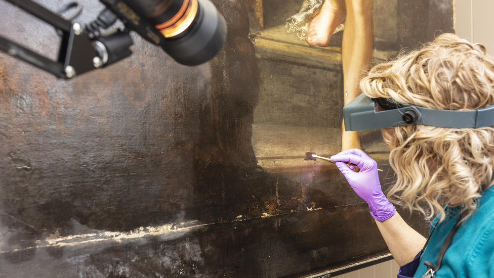 Conservator Adelaide Izat works on <em>Susanna and the Elders.</em> At this stage of the work, the painting's left half was still covered by dirt, overpaint and varnish.