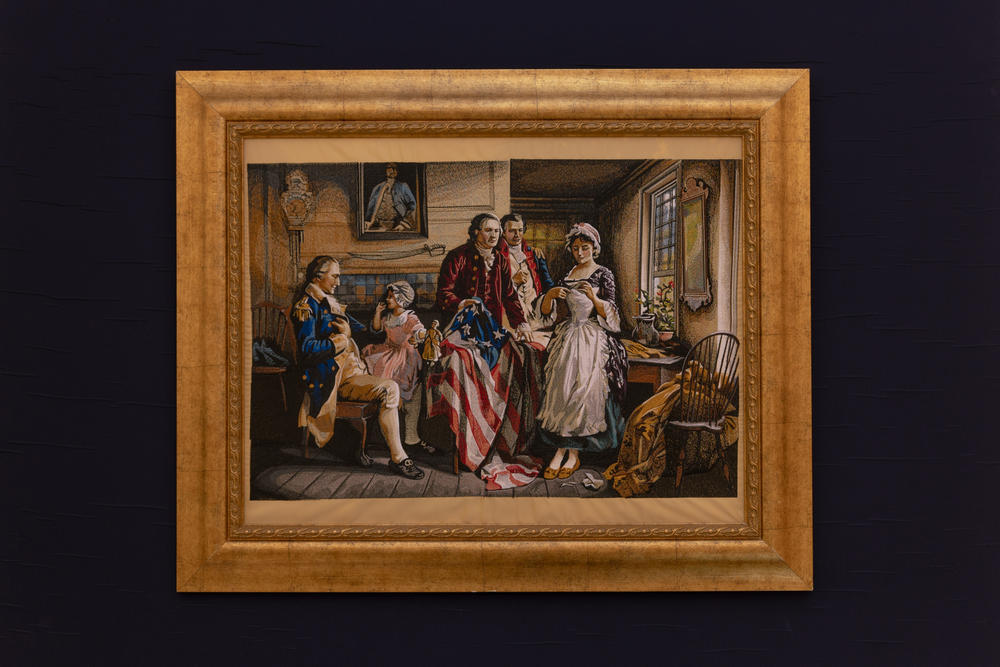 A framed machine-embroidered tapestry depicting historical flag embroidery is on display in the room.