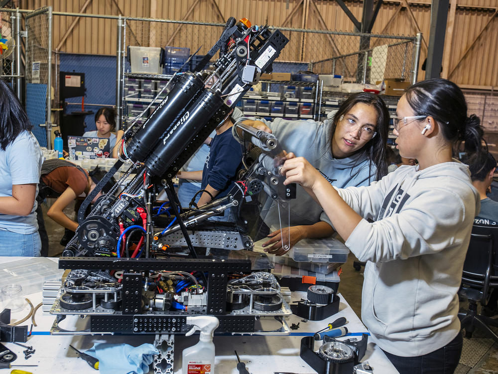 Claire Montegut (second from right), 16, and Anika Zhou (right), 17, are members of the Space Cookies, a <em>FIRST</em> Robotics Competition team composed of all Girl Scouts. Here they fix their robot's roller 