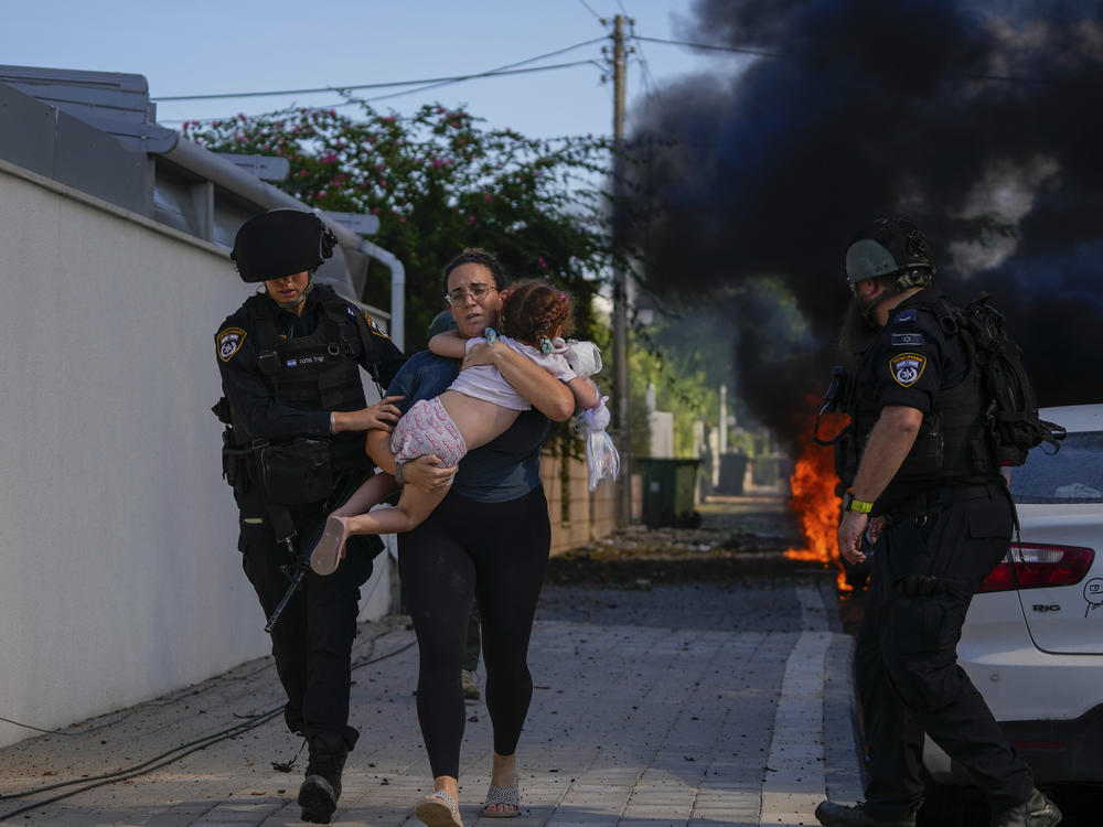 Israeli police officers evacuate a woman and a child from a site hit by a rocket fired from the Gaza Strip, in Ashkelon, southern Israel, on Saturday. The rockets were fired as Hamas announced a new operation against Israel.