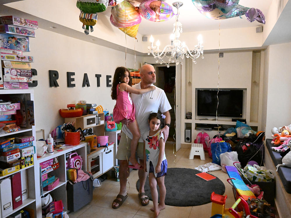 Ido Dan, an uncle to three children feared abducted by Hamas and taken to Gaza, stands for a portrait with his twin daughters. The remnants of their sixth birthday party, which took place the same day as the incursion, are still around the house.