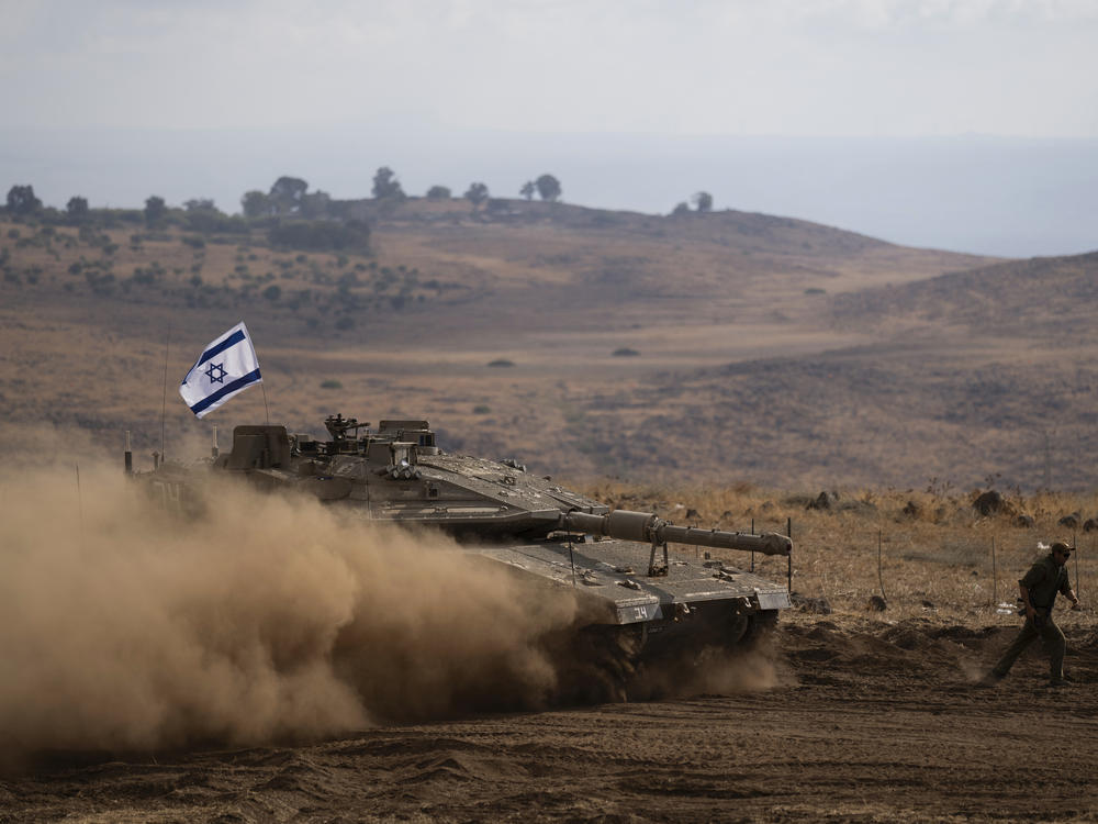 An Israeli soldier runs in front of a tank with an Israeli flag on the top in a staging area near the Israeli border with Lebanon on Sunday.