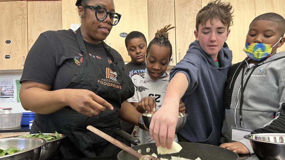 Students help instructional coach Regina Green caramelize onions for a dish featuring fresh greens from the school garden at Watkins Elementary.