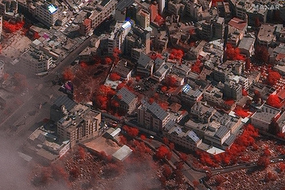 An infrared satellite image shows foliage, like trees, in red. The area burned by the explosion (center) appears relatively small, and structures at the hospital have not received significant damage.