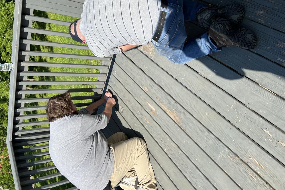 An incarcerated youth held at the Backbone Mountain Youth Center and a supervisor work on a deck as part of a community service project.