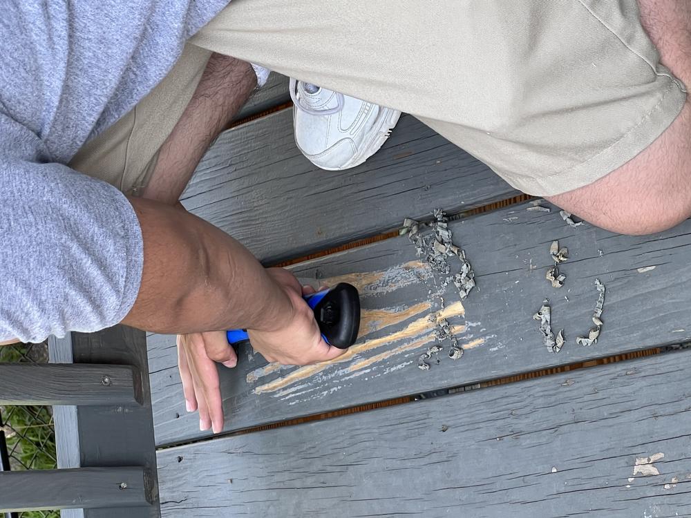 An incarcerated youth held at the Backbone Mountain Youth Center scrapes a deck as part of a community service project.