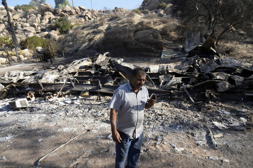 Luis Quinonez talks to a neighbor on the phone while surveying the damage to his property after the Highland Fire passed through Tuesday in Aguanga.