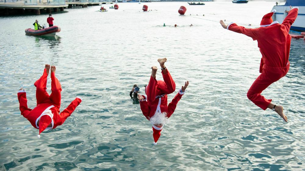 Participants sporting Santa Claus costumes jump into the water during the 111th edition of the Copa Nadal swimming race in Barcelona's Port Vell on December 25, 2020.