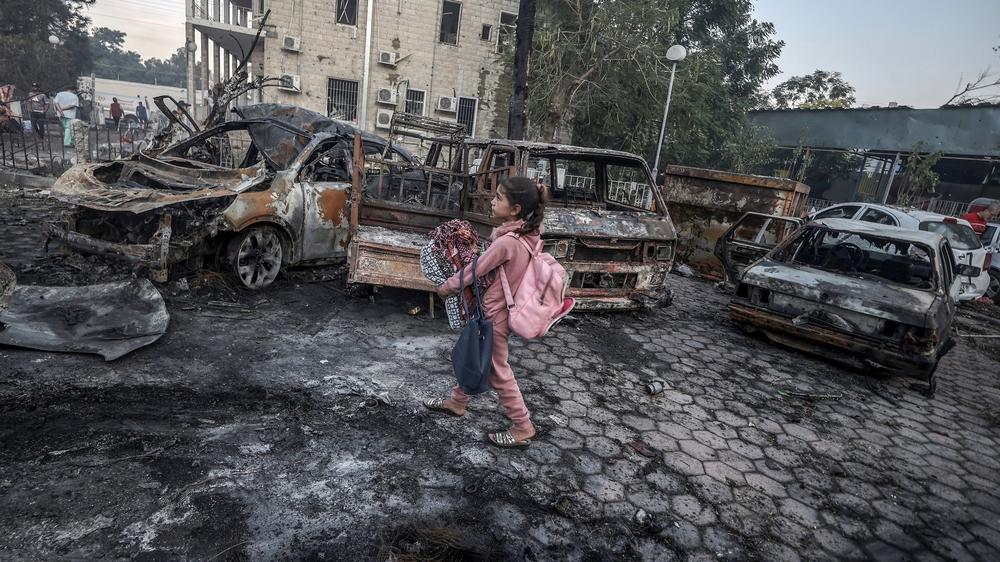 A girl tries to collect usable belongings amid the wreckage of vehicles after the explosion at Al Ahli Arab Hospital in Gaza.