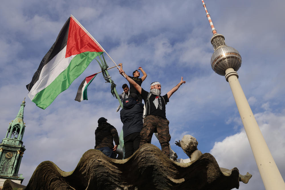 A man waves a Palestinian flag from atop Neptune Fountain during a 