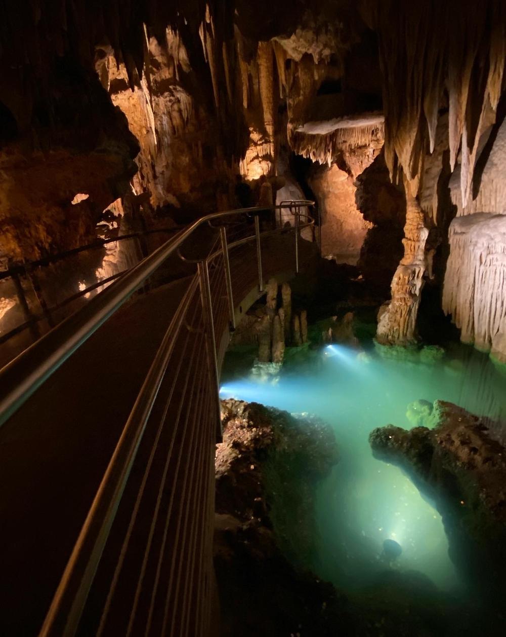 Pools of glassy, smooth water reflect the stalactites above. It creates the illusion of an underwater stone city.