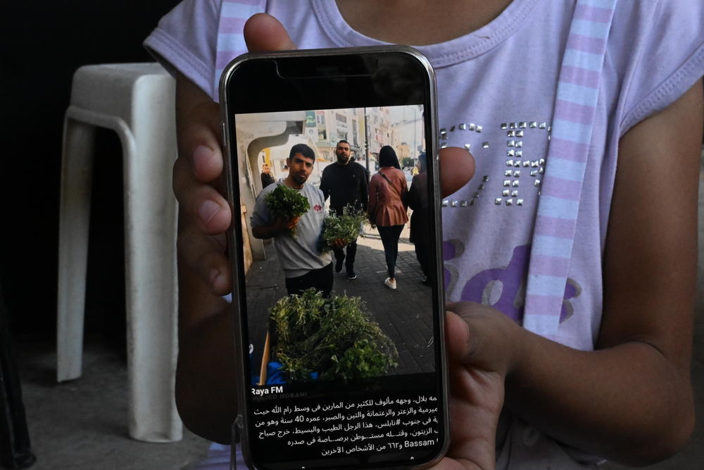 Bilal's daughter shows a photo of him on a phone.