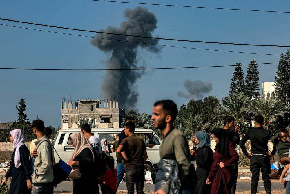 Smoke from Israeli bombardment rises behind people fleeing south from Gaza City and other parts of the northern Gaza Strip, as they walk along a highway on Nov. 9.