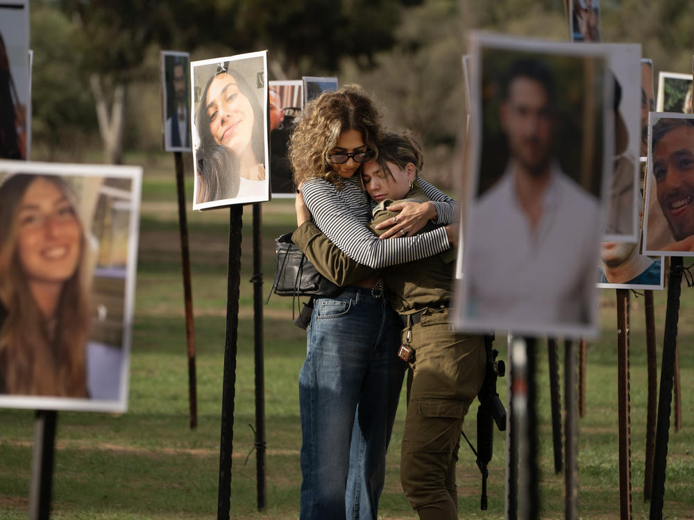 Sigal Manzuri, whose daughters Norelle and Roya were killed in the Hamas-led attack on the Nova music festival on Oct. 7, embraces one of their friends. Surrounding them are photos of people killed and taken hostage by Hamas militants, displayed at the site as DJs spin music to commemorate victims, near Kibbutz Re'im, Tuesday.