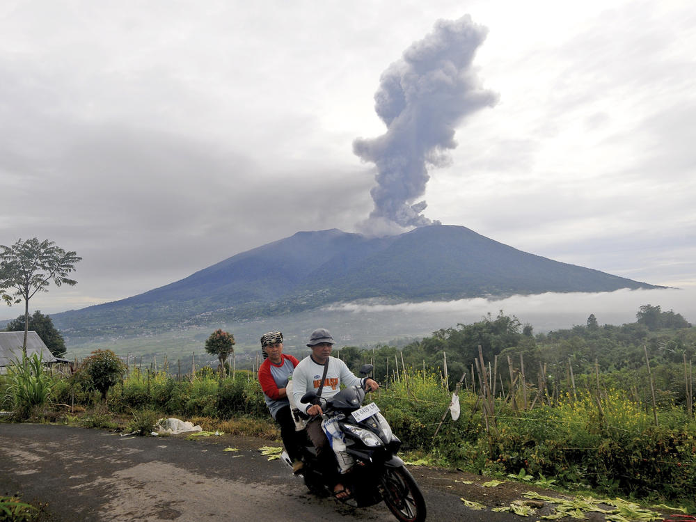 Motorists ride past by as Mount Marapi spews volcanic materials during its eruption in Agam, West Sumatra, Indonesia, Monday, Dec. 4, 2023.