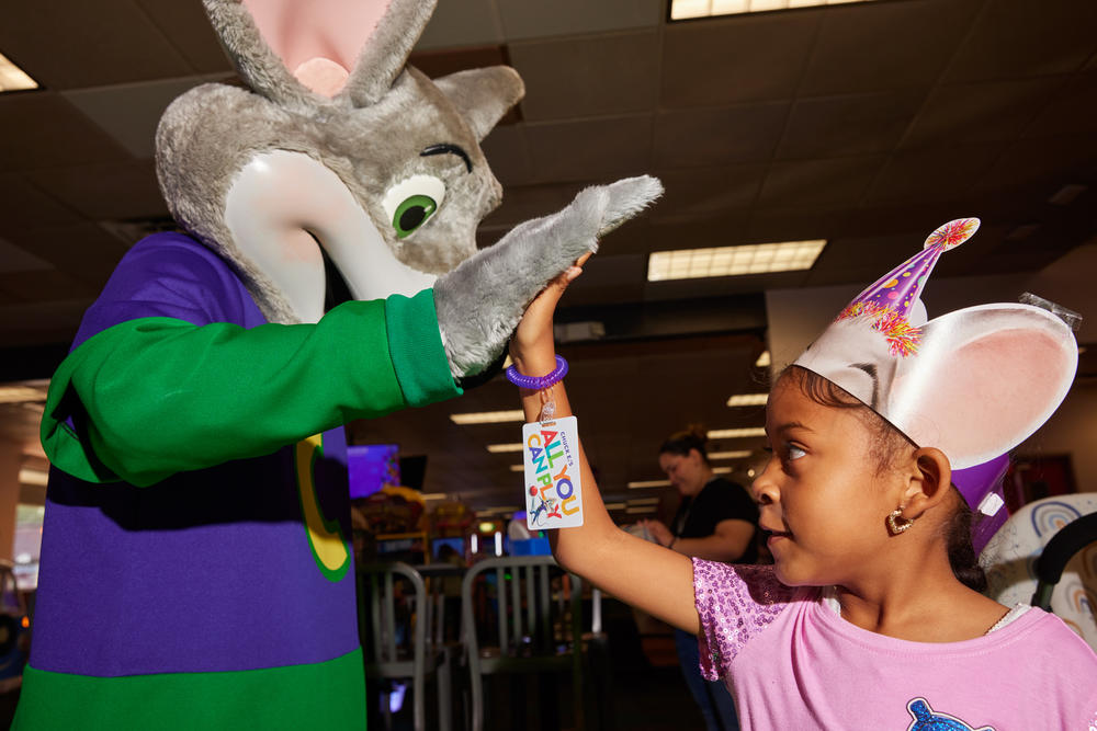 The walkaround Chuck E. Cheese costumed mascot gives Nia Thomas a high-five.