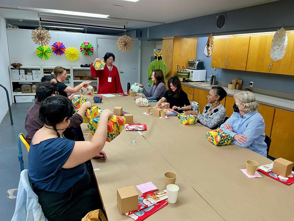 Tomoko Dyen (center) demonstrates how the furoshiki wrapping style creates easy to carry packages during a workshop she taught at the Craft Contemporary Museum in Los Angeles, Dec. 2, 2023.