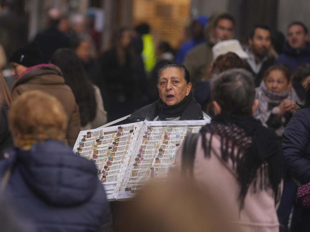 A Christmas lottery seller looks for customers in a crowded street in Madrid, Spain, Sunday, Dec. 3, 2023. (AP Photo/Paul White)