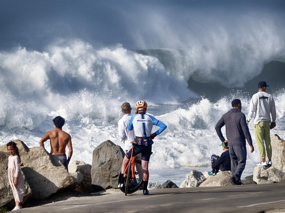 Beachgoers watch as turbulent surf pounds the coast on Thursday in Manhattan Beach, Calif.