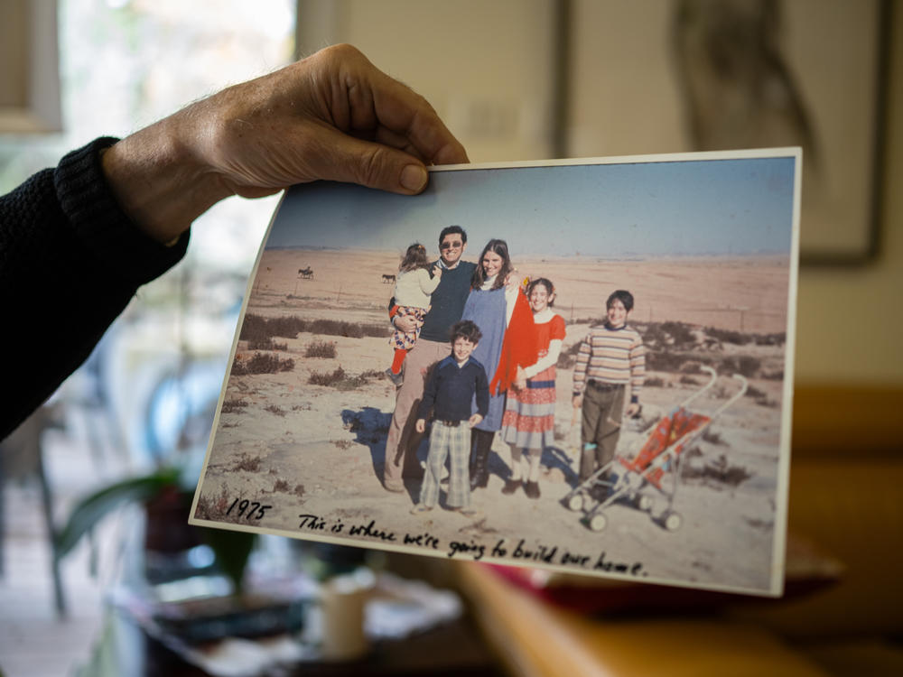 Ilan Troen displays a photo from 1975 of his family on the land where they built their home in Omer, Israel. In the photo, Troen holds his daughter Deborah when she was young. She was killed Oct. 7, 2023.