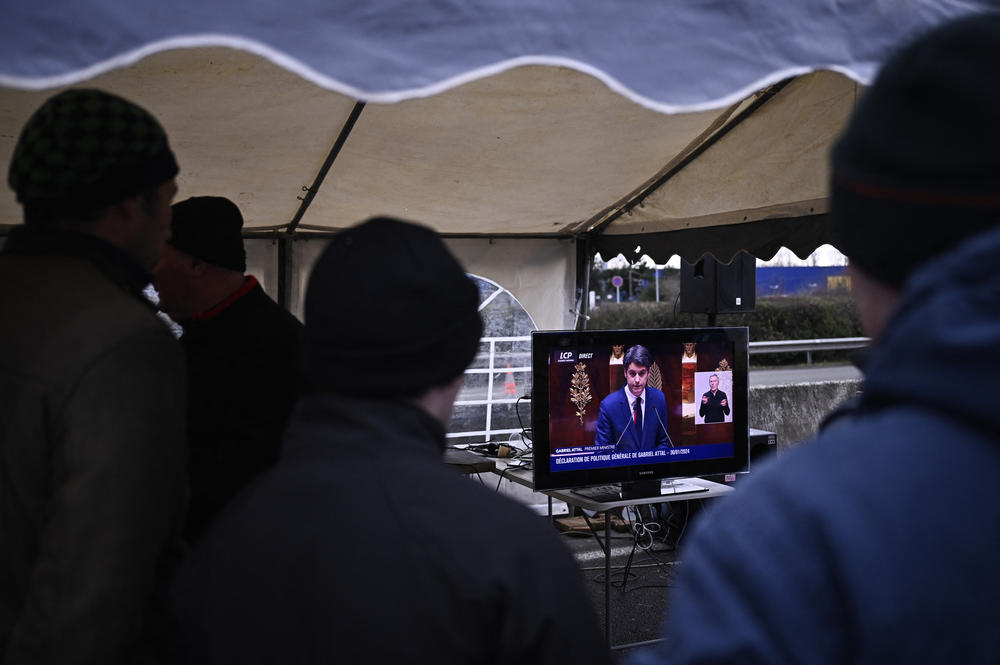 French farmers watch a broadcast of French Prime Minister Gabriel Attal delivering his government's policy statement at the National Assembly, as they take part in a roadblock protest on the A6 highway near Lisses, south of Paris.