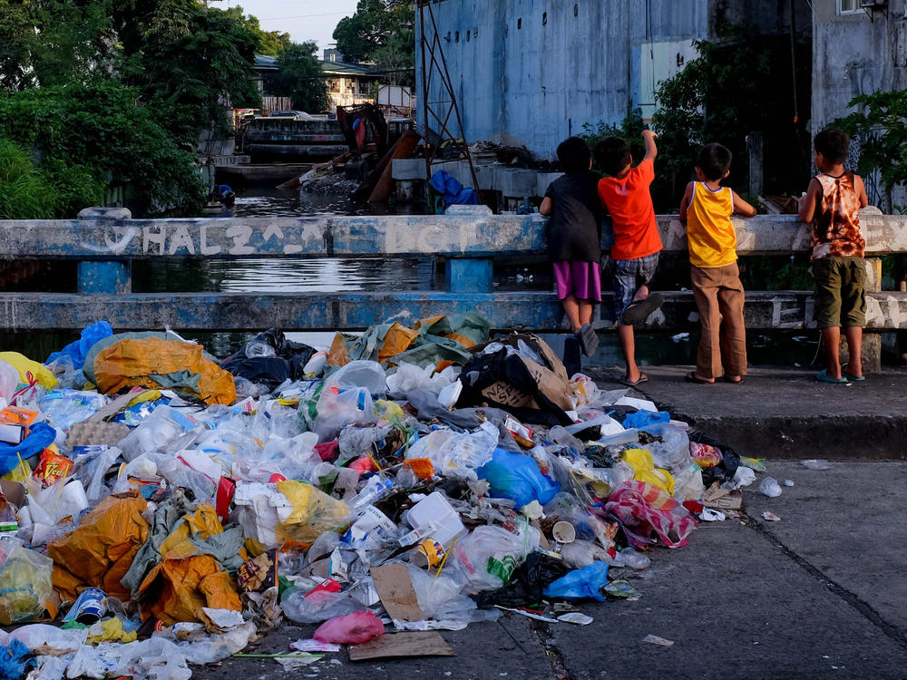 A pile of plastic waste and other garbage next to children playing on a bridge in the Philippines.