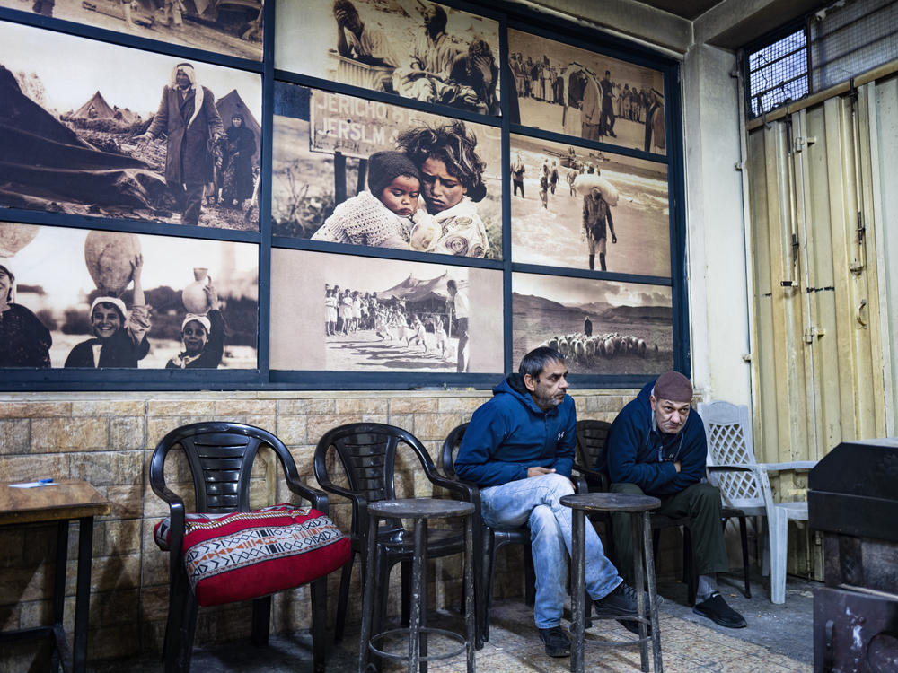 Inside a cafe in the Al Ama'ari refugee camp in the occupied West Bank, men huddle around a wooden stove for warmth in front of a large mural of photographs from 1948, when many Palestinians were forcibly displaced from their homes.
