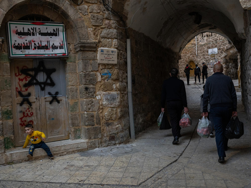 Palestinians walk by a door that was spray painted with a Star of David in the old city of Hebron.