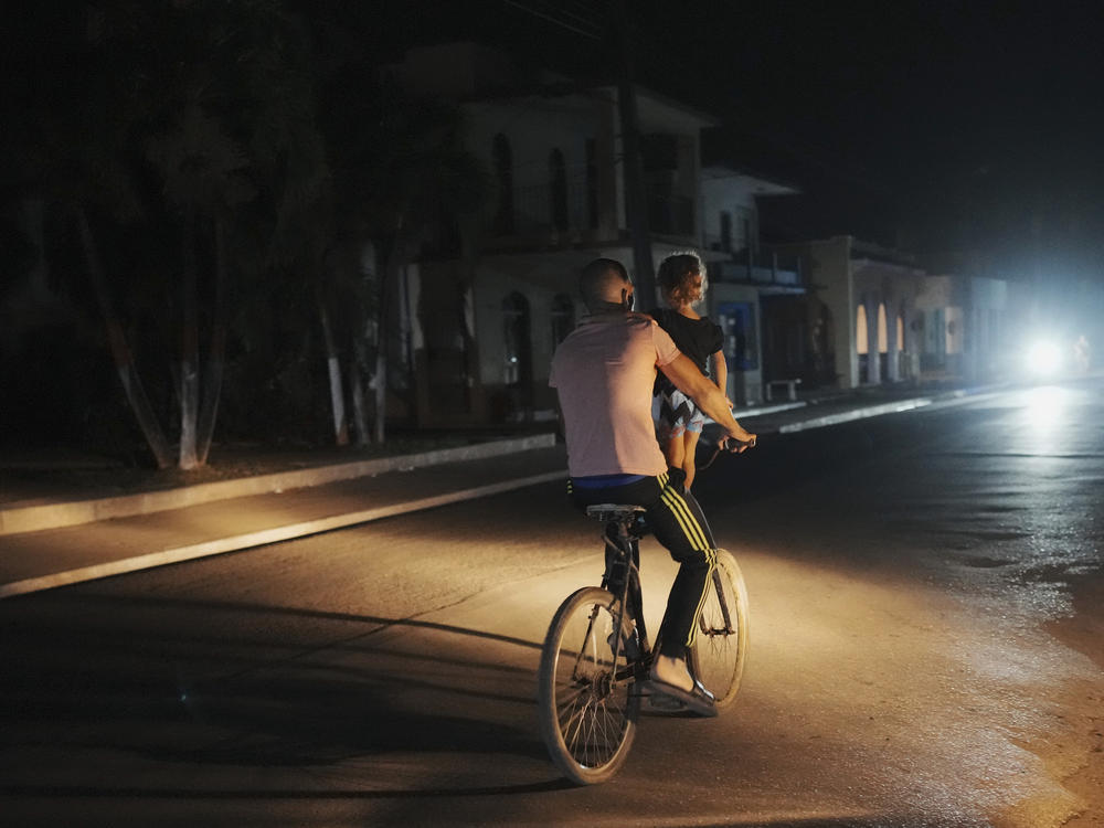 A a man pedals carrying a girl during a scheduled power outage in Bauta, Cuba, Monday, March 18. The island is facing an energy crisis, with waves of blackouts worsening in recent weeks.
