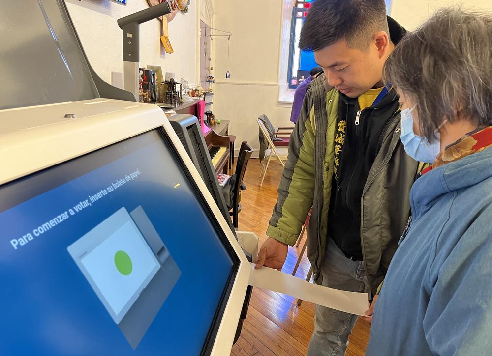 Wei Chen, left, civic engagement director at Asian Americans United, inserts a sample paper ballot to demonstrate how to use a voting machine at 99 Adult Day Care II, an adult day care center in Philadelphia that supports Chinese speakers.