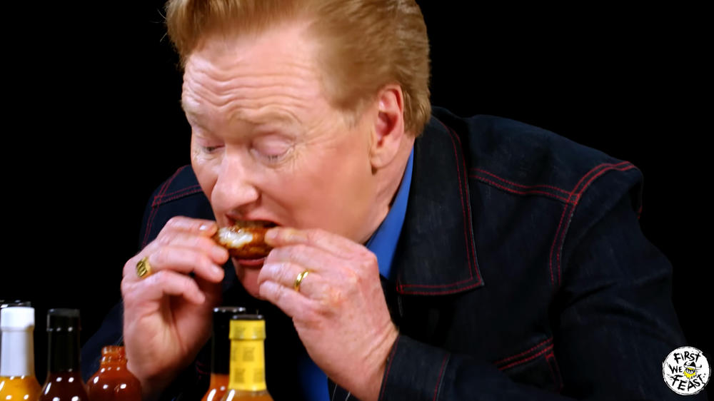 Conan O'Brien eats a chicken wing during his Hot Ones interview.