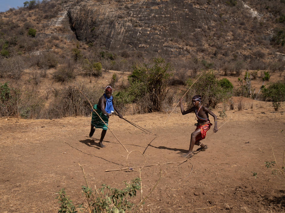 In the afternoon, when the work is done, the boys entertain themselves with an ancient game — throwing spears through a rolling hoop.