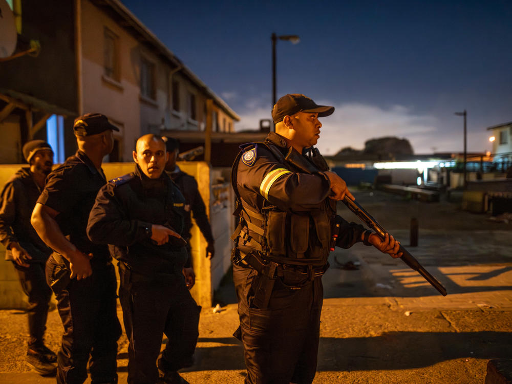 Law enforcement officers react during a standoff with suspected gang members in the Woodlands neighborhood of Cape Town, South Africa. Police officers regularly come under fire while working in high-crime areas in the Cape Flats.